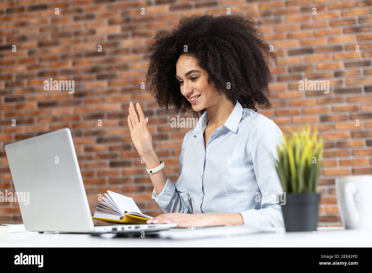 Donna d'affari afroamericana sorridente in abiti casual con capelli afro seduto alla scrivania, studiare o lavorare online, avendo una riunione virtuale Foto Stock