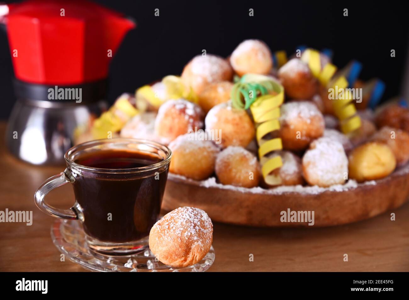 Il caffè espresso viene versato da una macchina per caffè geyser. castagnole al forno con zucchero in polvere. Dolci tradizionali in mano. Street food, biscotti rotondi con zucchero per il carnevale di Venezia. Foto Stock