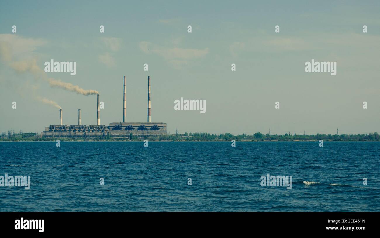 Centrale termica. Impresa industriale vicino al laghetto, che emette costantemente fumo e aumenta l'inquinamento ambientale Foto Stock