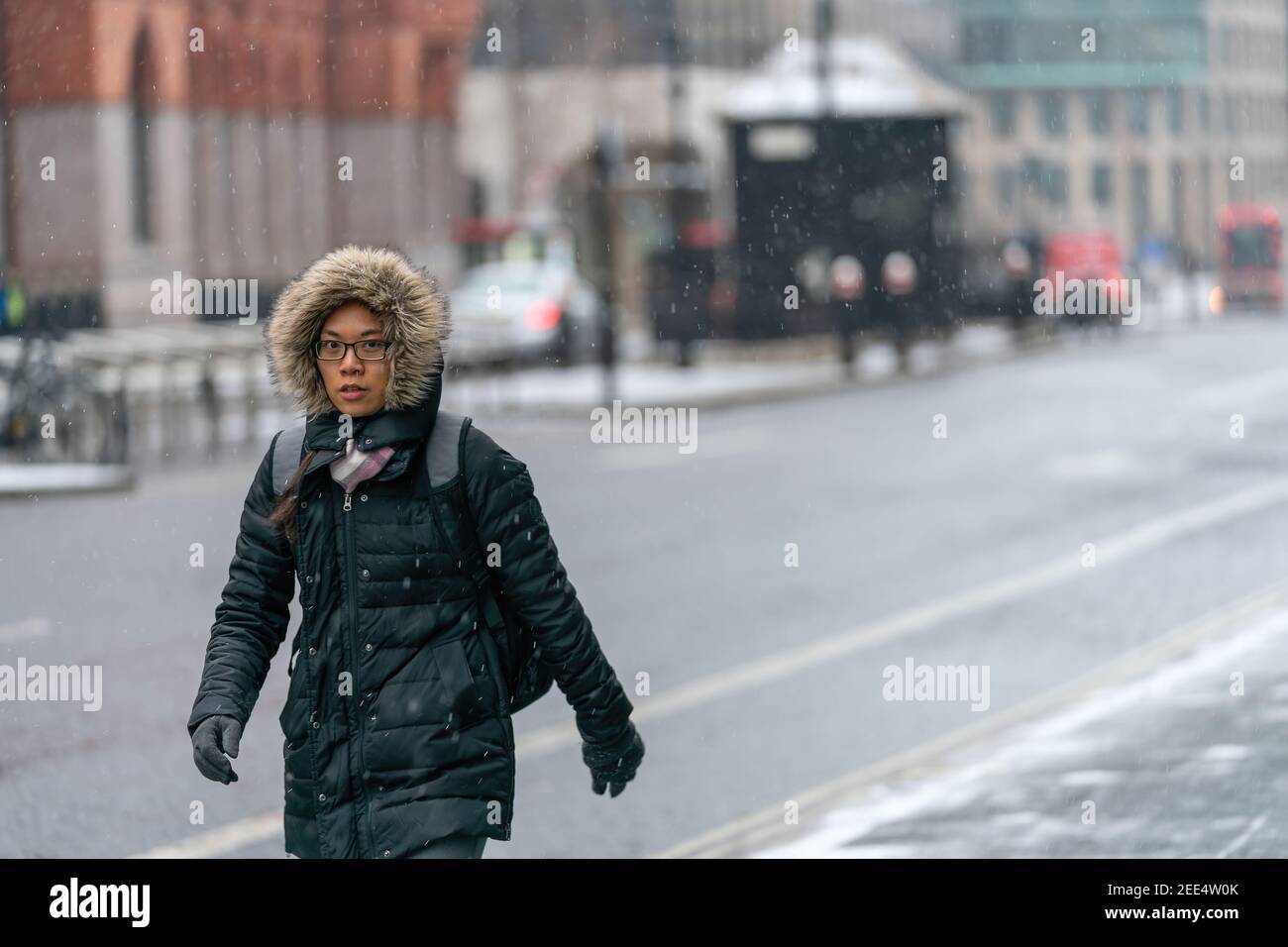 LONDRA, INGHILTERRA - 8 FEBBRAIO 2021: Bella giovane donna orientale in un cappuccio rivestito di pelliccia che indossa occhiali che camminano in doccia di neve in Holborn Londra su Foto Stock