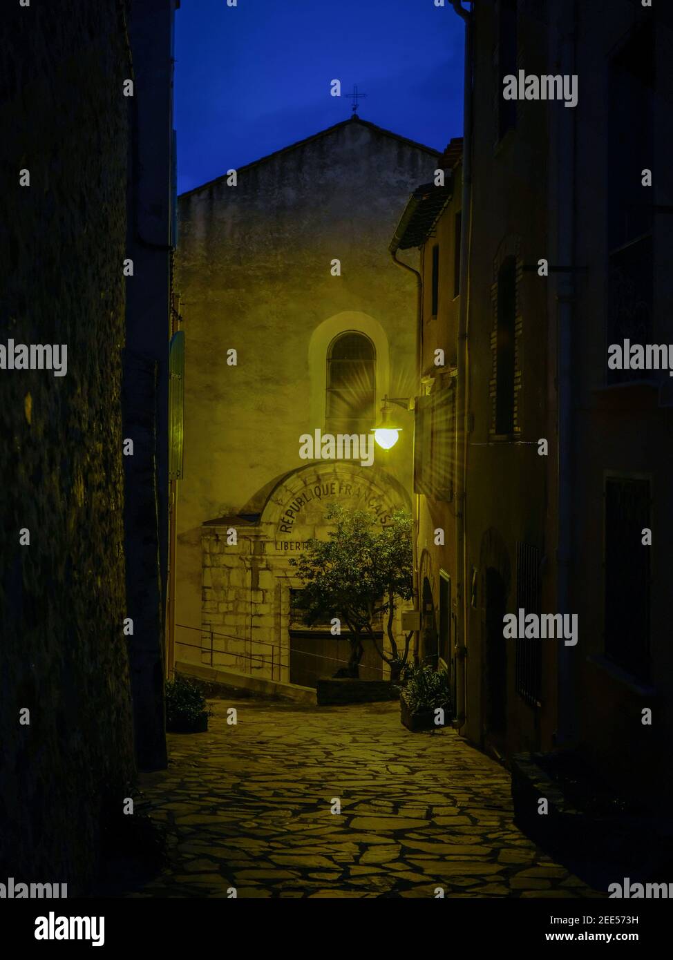 Facciata della chiesa in serata con un unico apparecchio luminoso esterno che diffonde una luce gialla. Preso a Collioure, Francia nel mese di dicembre. Foto Stock