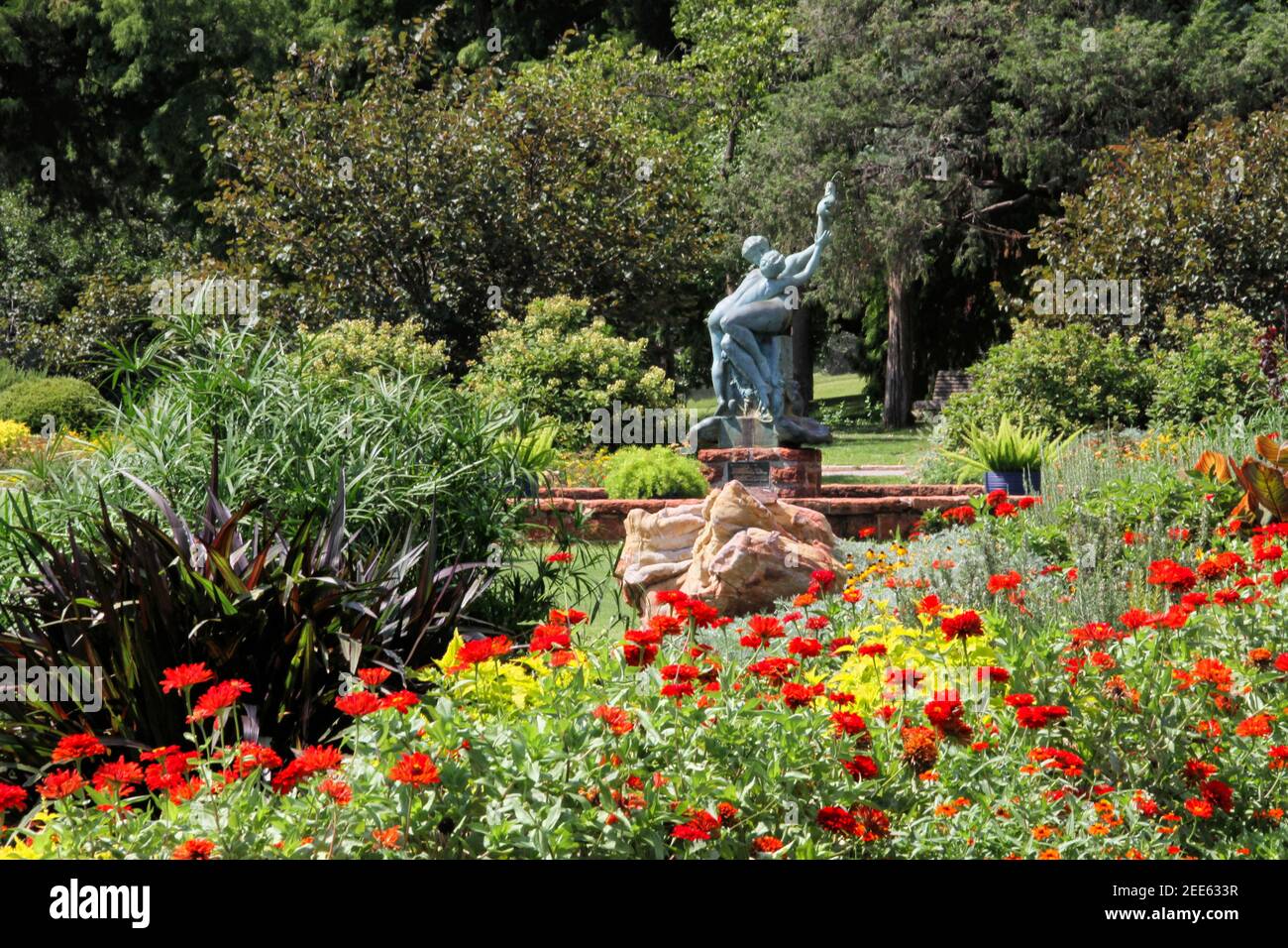 Il Will Rogers Park Botanical Garden di Oklahoma City mostra le zinnie rosse con l'iconica fontana di madre e bambino che tiene un pesce sullo sfondo. Foto Stock