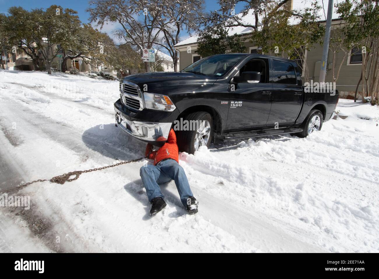 Austin, TX 15 febbraio 2021: Un automobilista il cui camion è rimasto bloccato nella neve cerca di agganciare una catena ad esso nel centro di Austin dopo una rara tempesta di neve ha scaricato più di sei pollici di neve durante la notte nel Texas centrale. Le strade di tutta la città erano impraticabili per la maggior parte dei veicoli senza capacità di trazione integrale. Credit: Bob Daemmrich/Alamy Live News Foto Stock