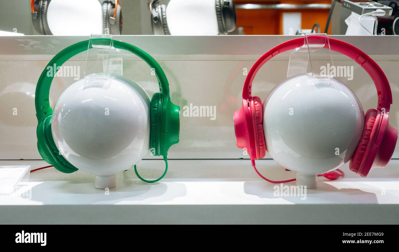 Cuffie rosse e verdi su manichini, in una vetrina di elettronica e tecnologia digitale. Primo piano. Oggetti sferici su cui devono essere collegati i dispositivi audio Foto Stock