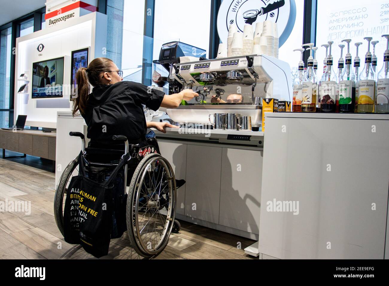 MINSK, BIELORUSSIA - Gennaio 2021: Una persona con disabilità su sedia a rotelle lavora come barista in una caffetteria inclusa. Il barista prepara il caffè nella sua caffetteria al lavoro. Un progetto unico, una caffetteria inclusiva. Un luogo in cui tutti i dipendenti sono disabilitati. Gestito da una persona con sindrome di Down. Tutti i baristi sono disattivati. Questo è Natasha Astanina. Ha 25 anni. È un utente della sedia a rotelle fin dall'infanzia. Il barista funziona. È stato impegnato nella danza sportiva dall'età di 13. È appassionato di paracadutismo. Per 10 salti di paracadute. Foto Stock