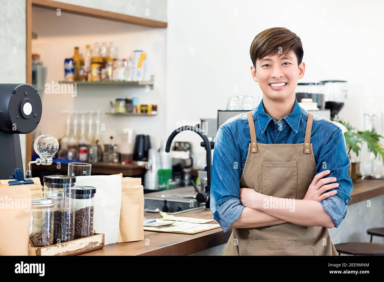 Allegro giovane imprenditore asiatico uomo in piedi al banco nel suo caffetteria privata Foto Stock