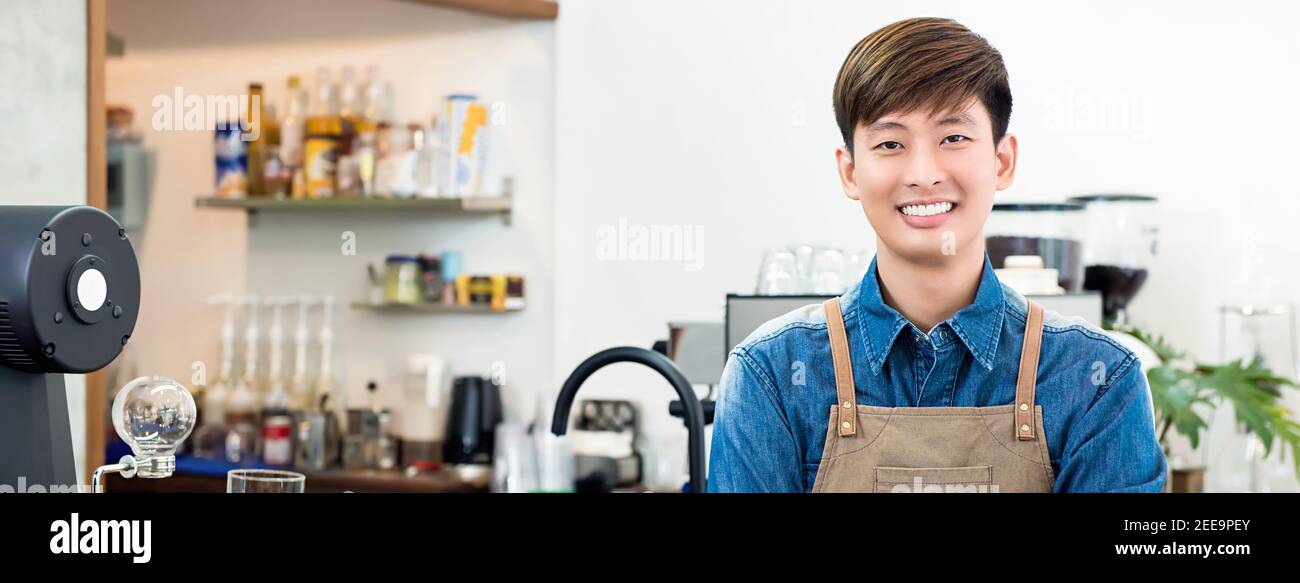 Allegro giovane imprenditore asiatico uomo in piedi al bancone nel suo proprio bar, banner panoramico Foto Stock