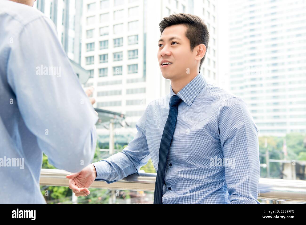Bell'uomo d'affari cinese asiatico che parla con colleghi all'aperto nel città con uffici in background Foto Stock