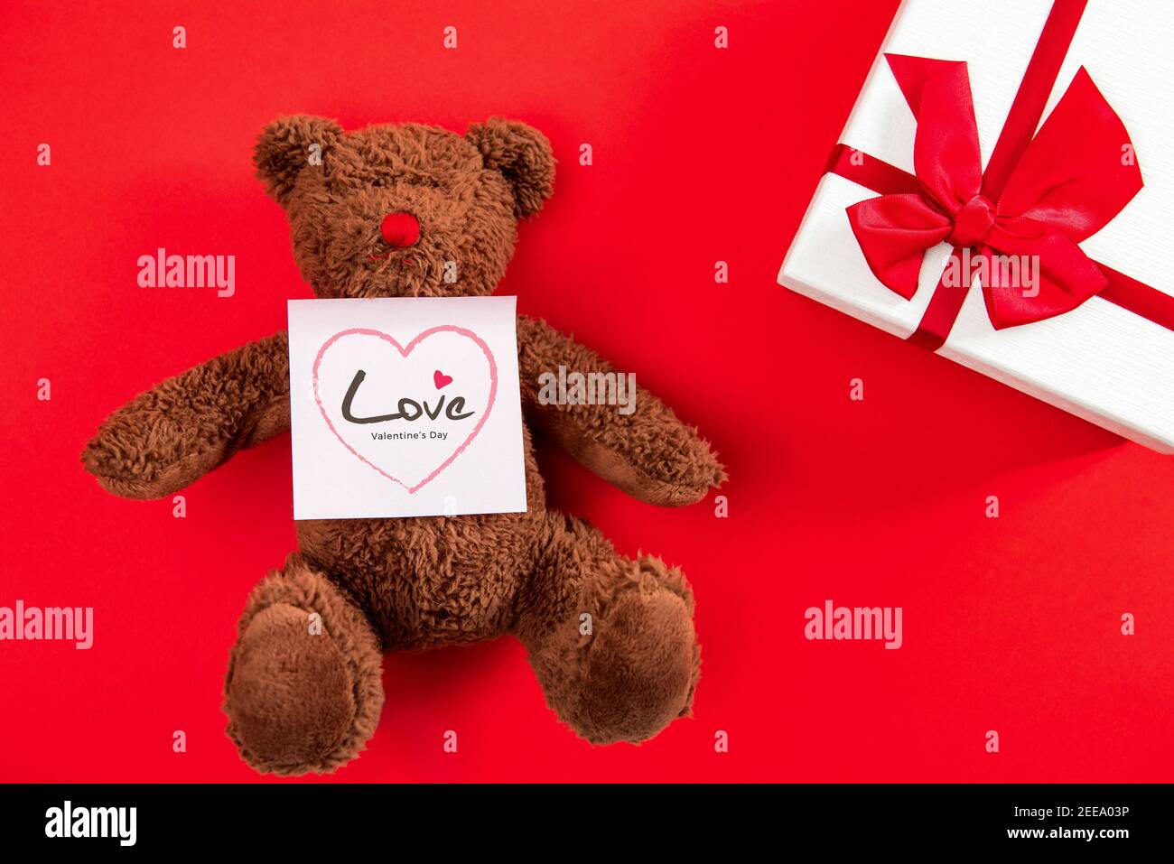 Confezione regalo per San Valentino e un simpatico giocattolo con la bambola dell'orso Messaggio di saluto Love in blocco note su sfondo rosso Foto Stock