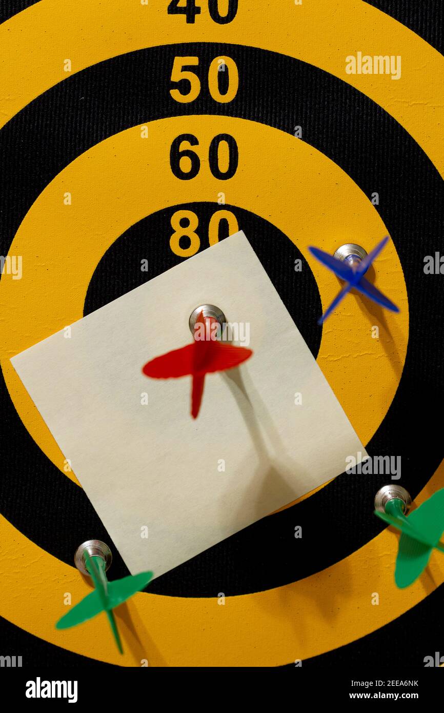 Una tavola a freccette con più frecce. La freccia rossa colpisce il bullseye. Una carta bianca (nota adesiva) si trova sotto la freccia vincente. Un'immagine personalizzabile Foto Stock
