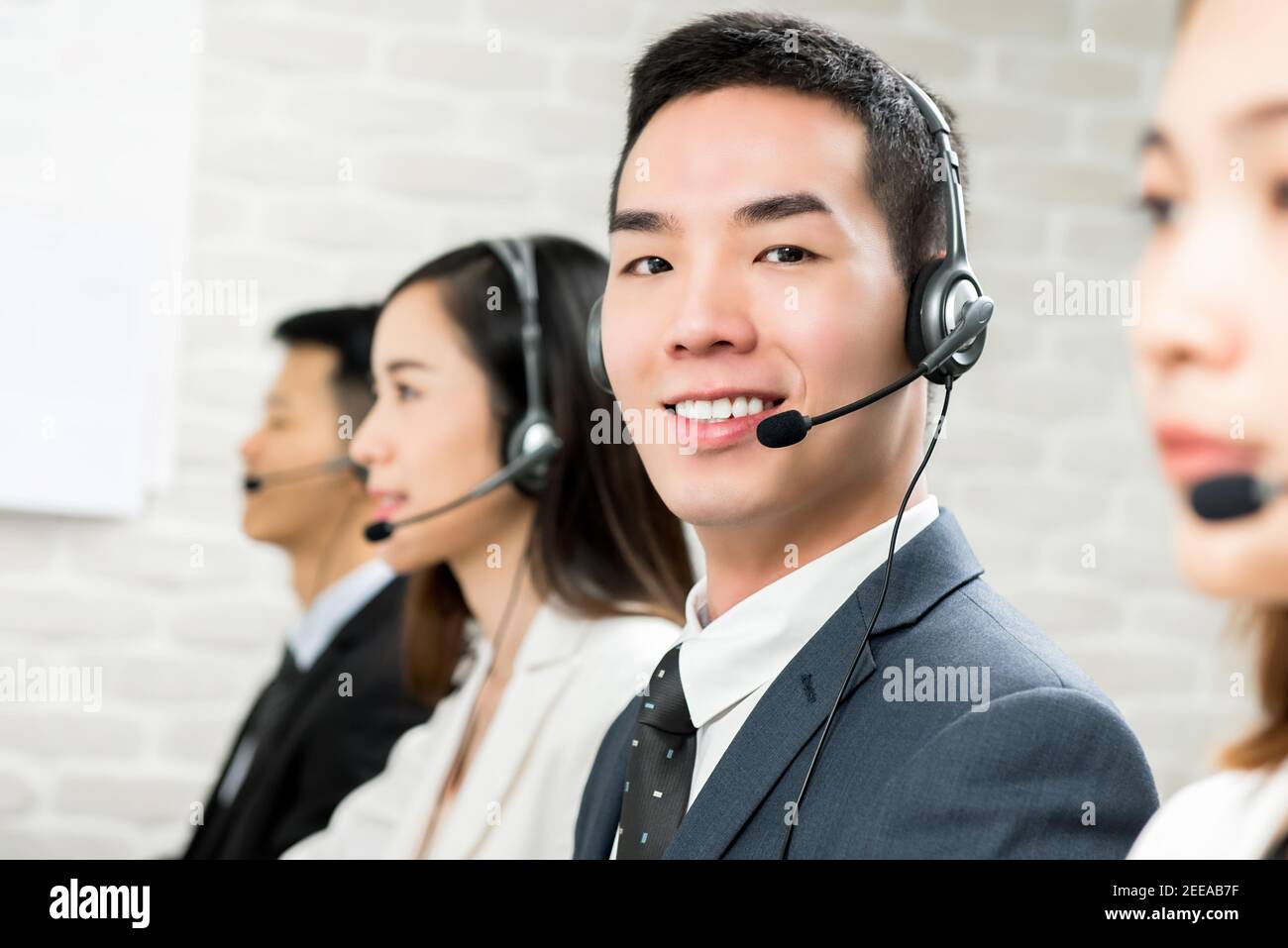 Sorridente agente di telemarketing per il servizio clienti asiatico di sesso maschile che lavora in chiamata centrare con il suo team Foto Stock