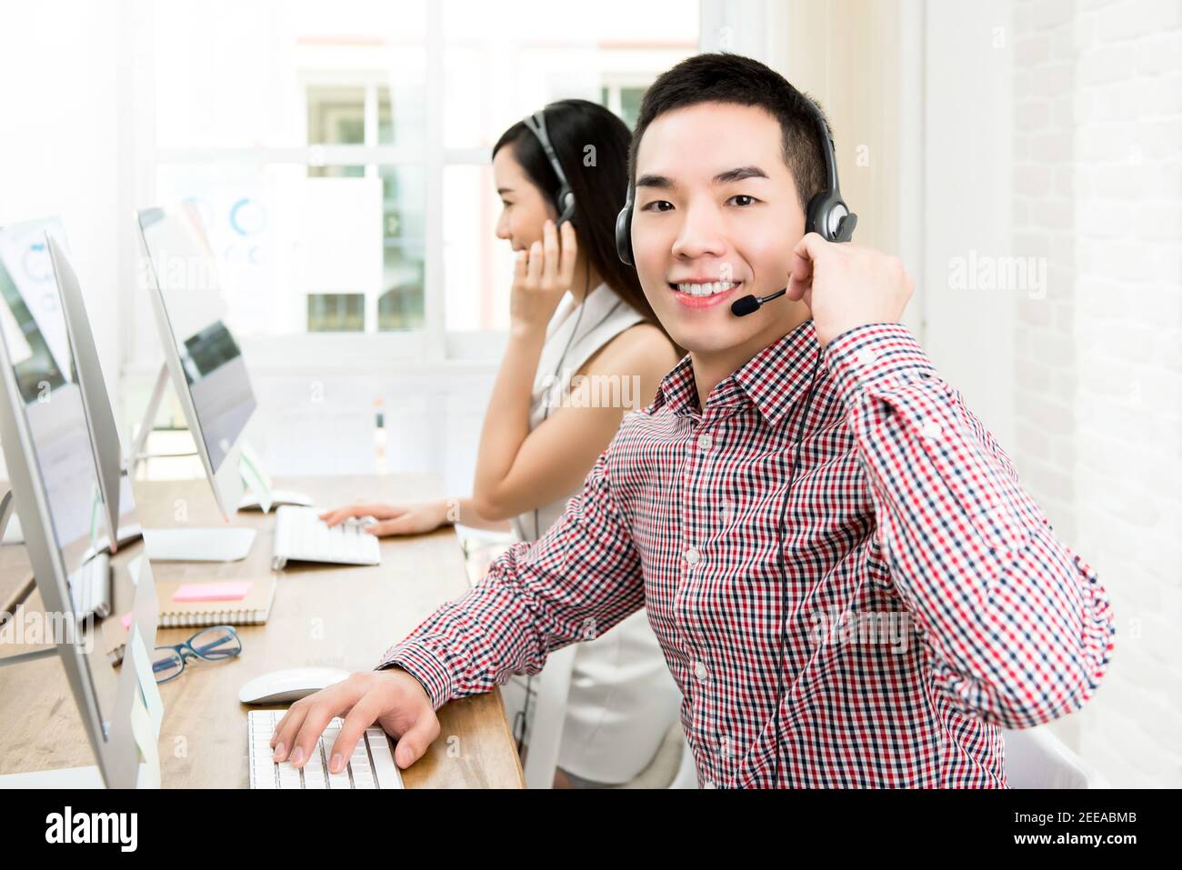 Smiling casual maschile asiatico servizio di telemarketing agente di lavoro in call center con il suo team Foto Stock