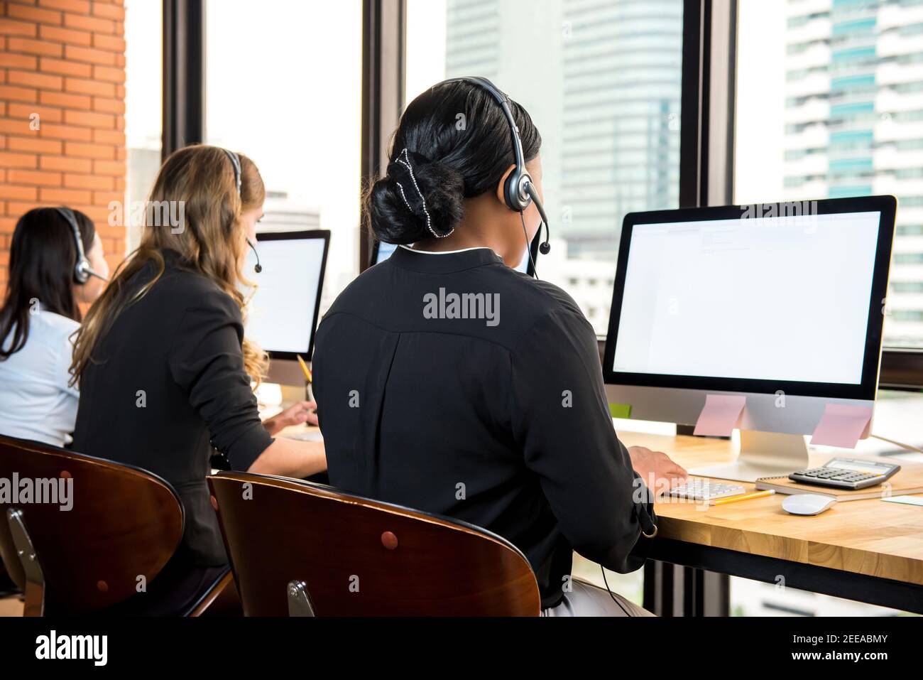 Donne d'affari che indossano le cuffie che lavorano sui computer come agenti di telemarketing Foto Stock