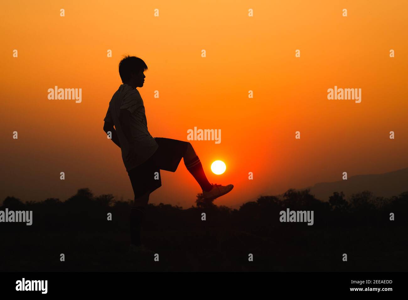 Silhouette sport d'azione all'aperto di un giovane che si diverte giocando a calcio per allenarsi nella zona rurale della comunità sotto il tramonto al crepuscolo. Foto Stock