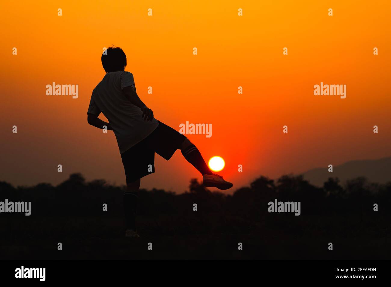 Silhouette sport d'azione all'aperto di un giovane che si diverte giocando a calcio per allenarsi nella zona rurale della comunità sotto il tramonto al crepuscolo. Foto Stock