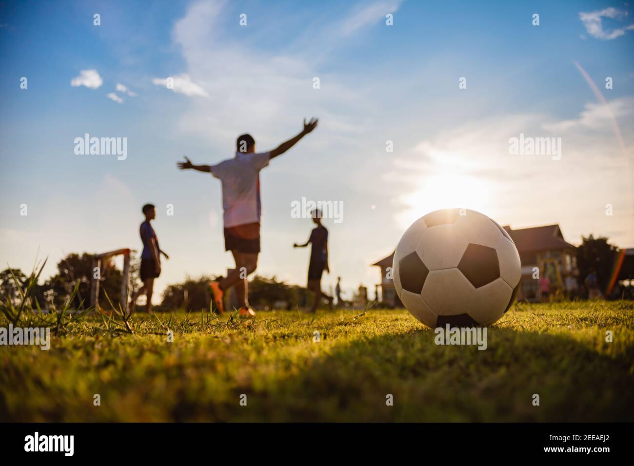 Silhouette sport d'azione all'aperto di un gruppo di bambini che si divertono giocando a calcio per allenarsi nella zona rurale della comunità sotto il tramonto al crepuscolo. Foto Stock