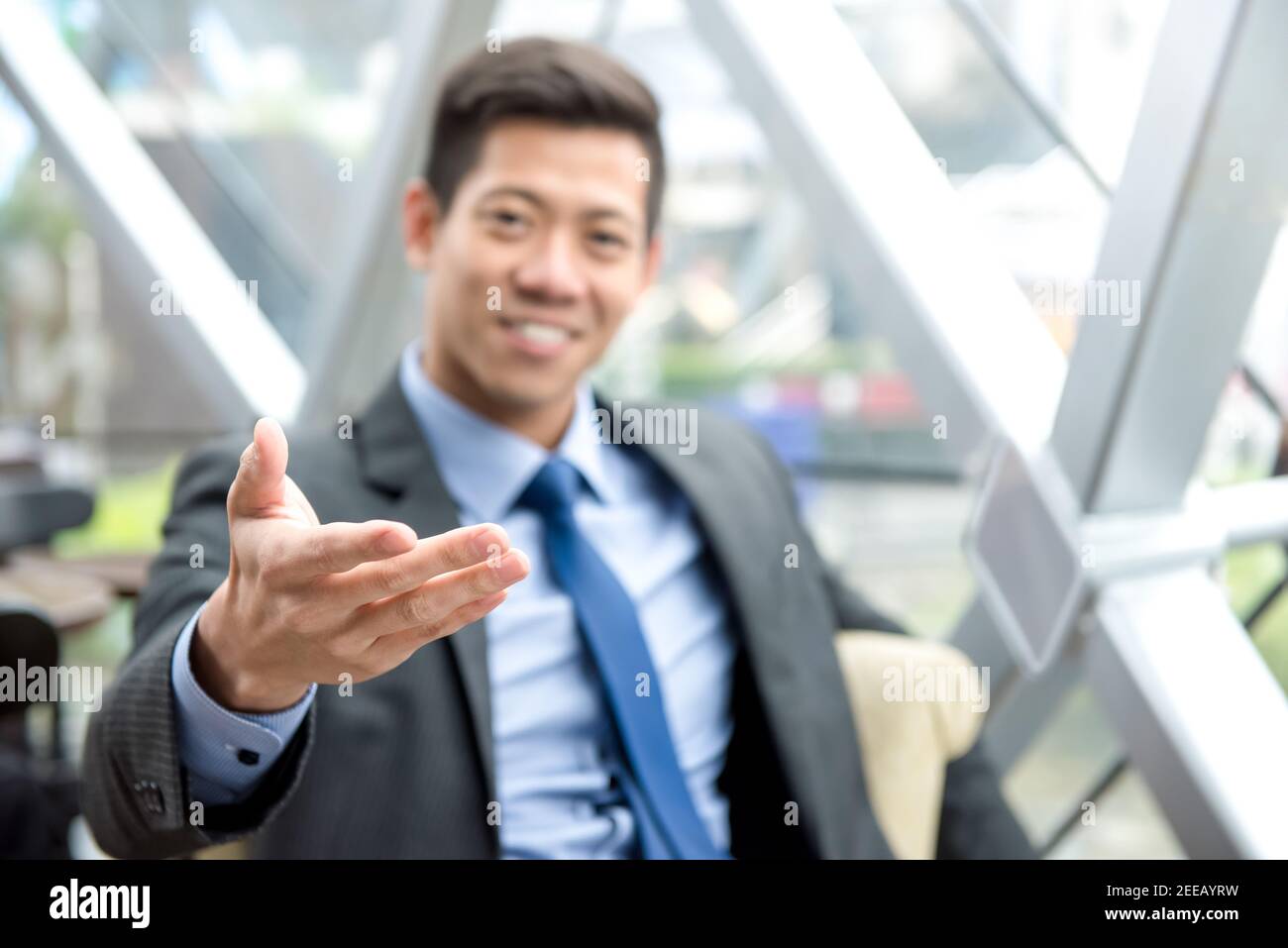 Accogliente uomo d'affari asiatico seduto nella sala d'ufficio che si apre mano con palma aperta, gesto di benvenuto Foto Stock
