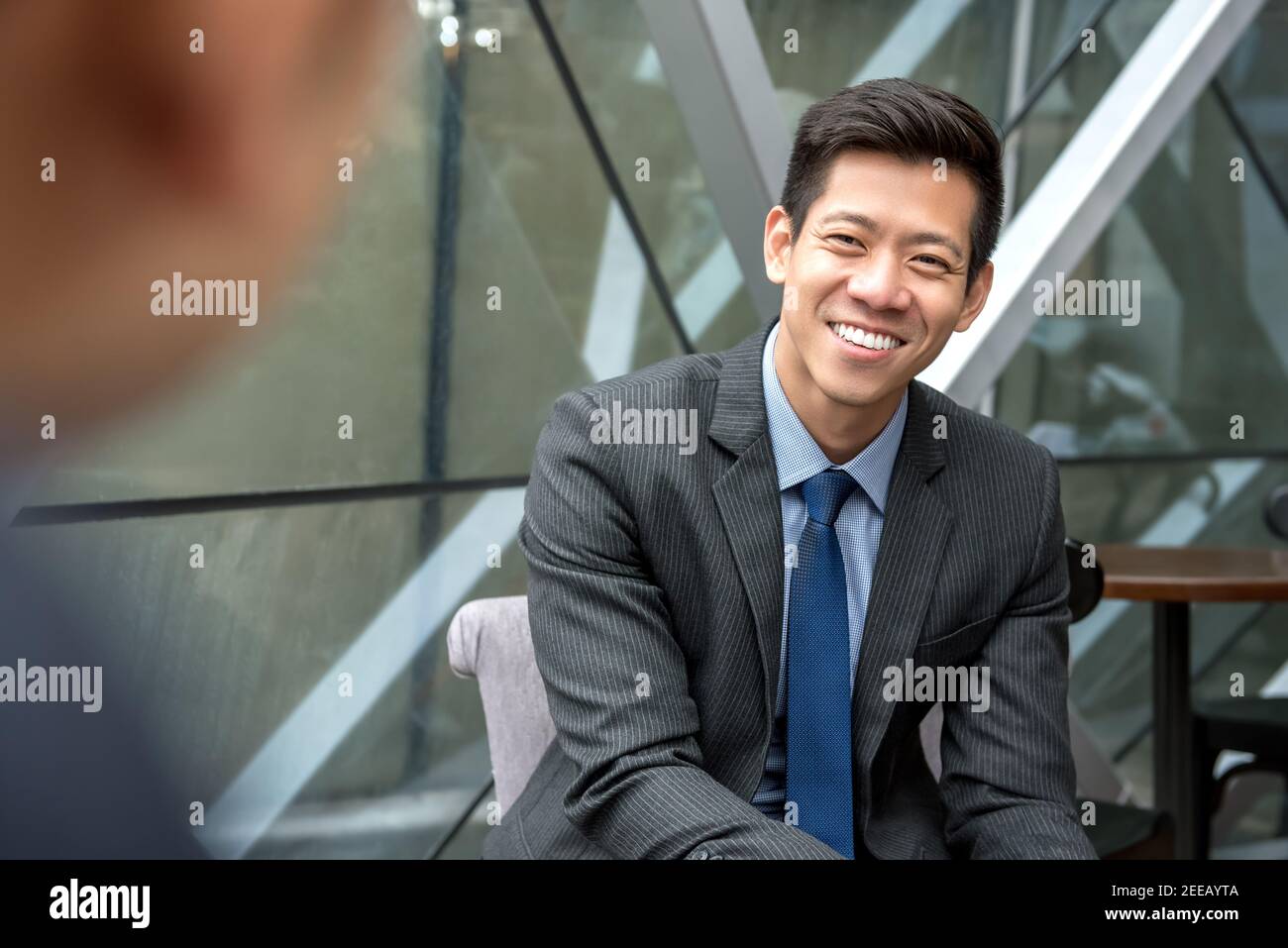 Cordiale e sorridente bell'uomo d'affari asiatico seduto in ufficio sala che parla con il suo collega Foto Stock
