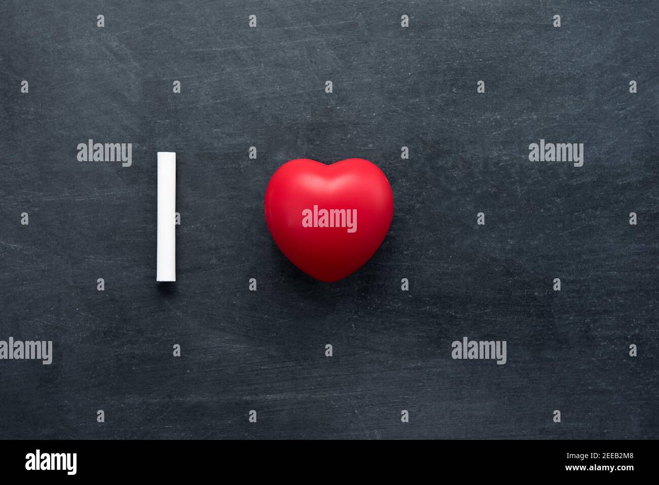 Gesso bianco con pallina rossa a forma di cuore che rappresenta l'amore, su sfondo lavagna con spazio vuoto Foto Stock