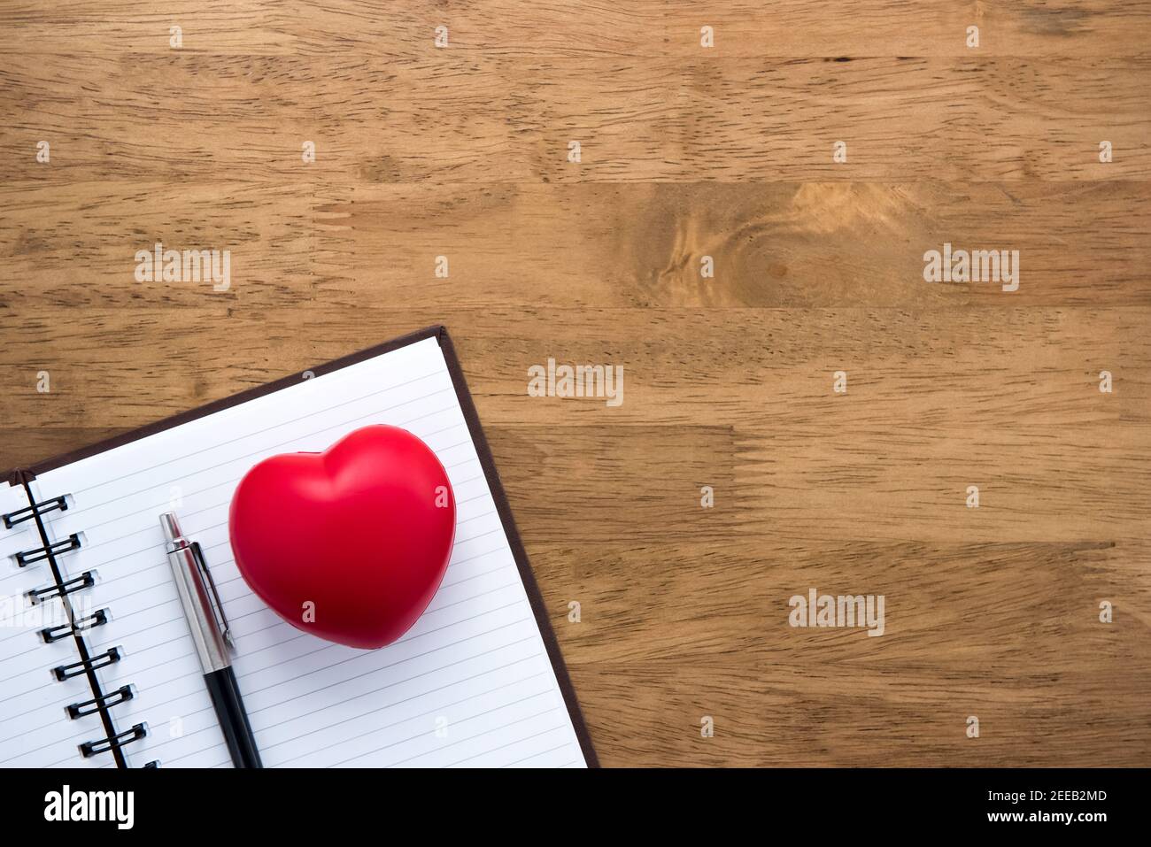 Notebook vuoto aperto con penna e sfera a forma di cuore sullo sfondo del tavolo in legno, vista dall'alto Foto Stock