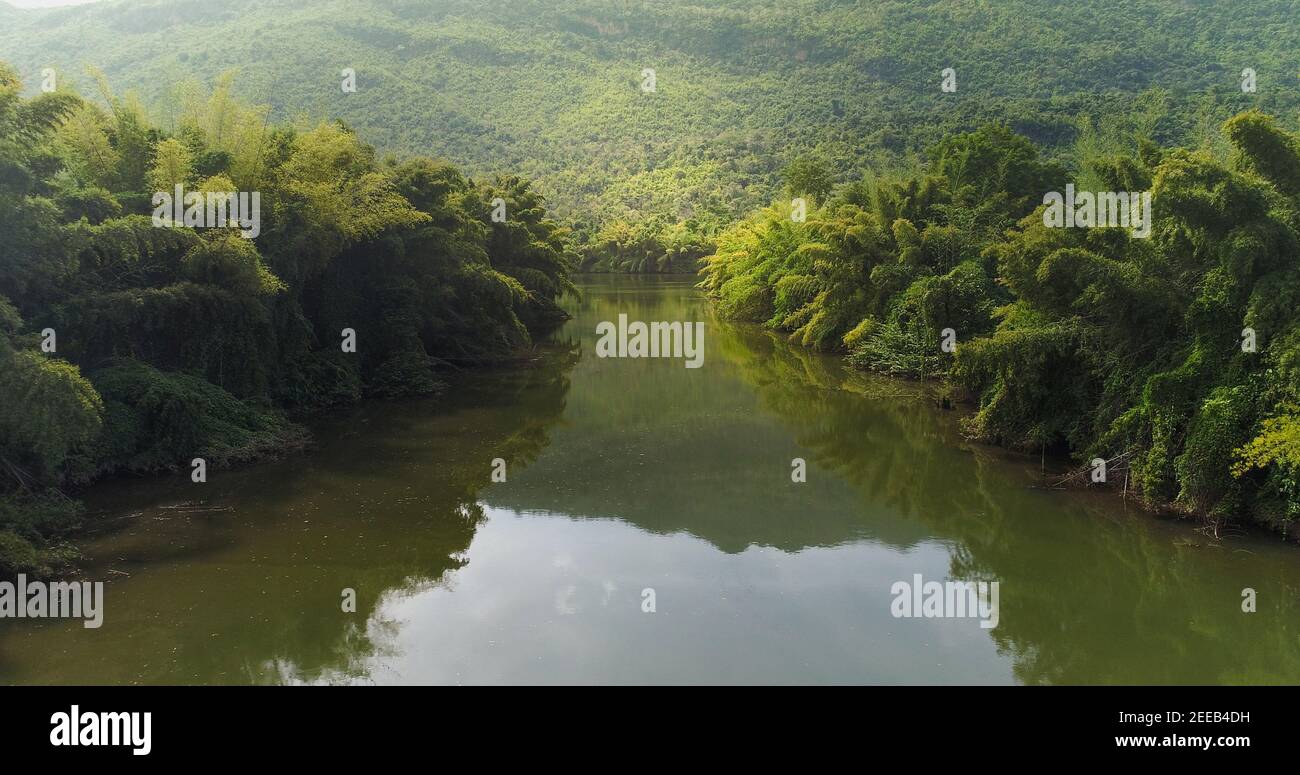Splendido paesaggio naturale del fiume in foresta tropicale verde con alberi su due lati e montagna sullo sfondo Foto Stock