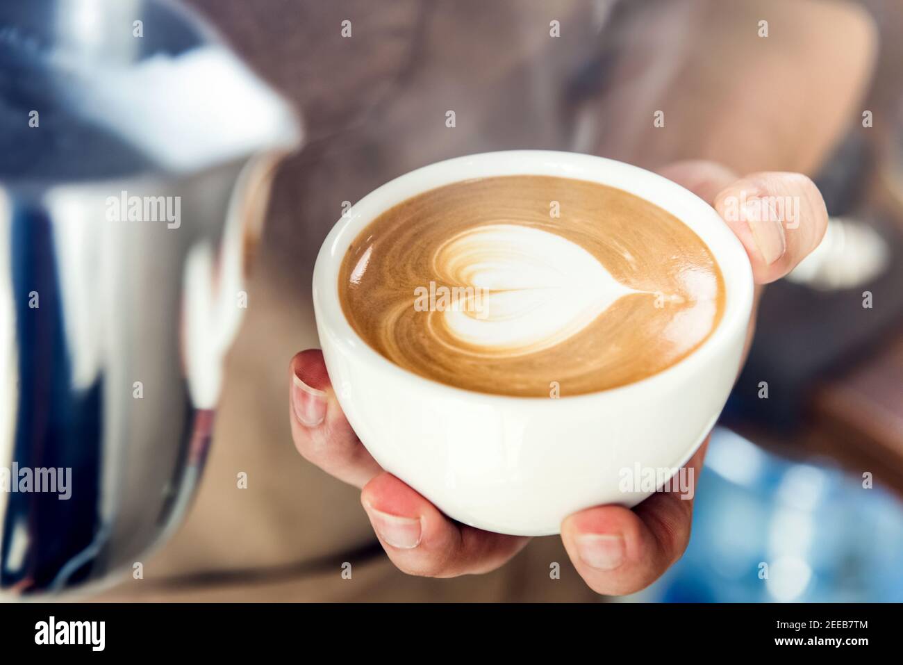 Barista professionista che tiene una tazza da caffè, per un latte a forma di cuore arte Foto Stock