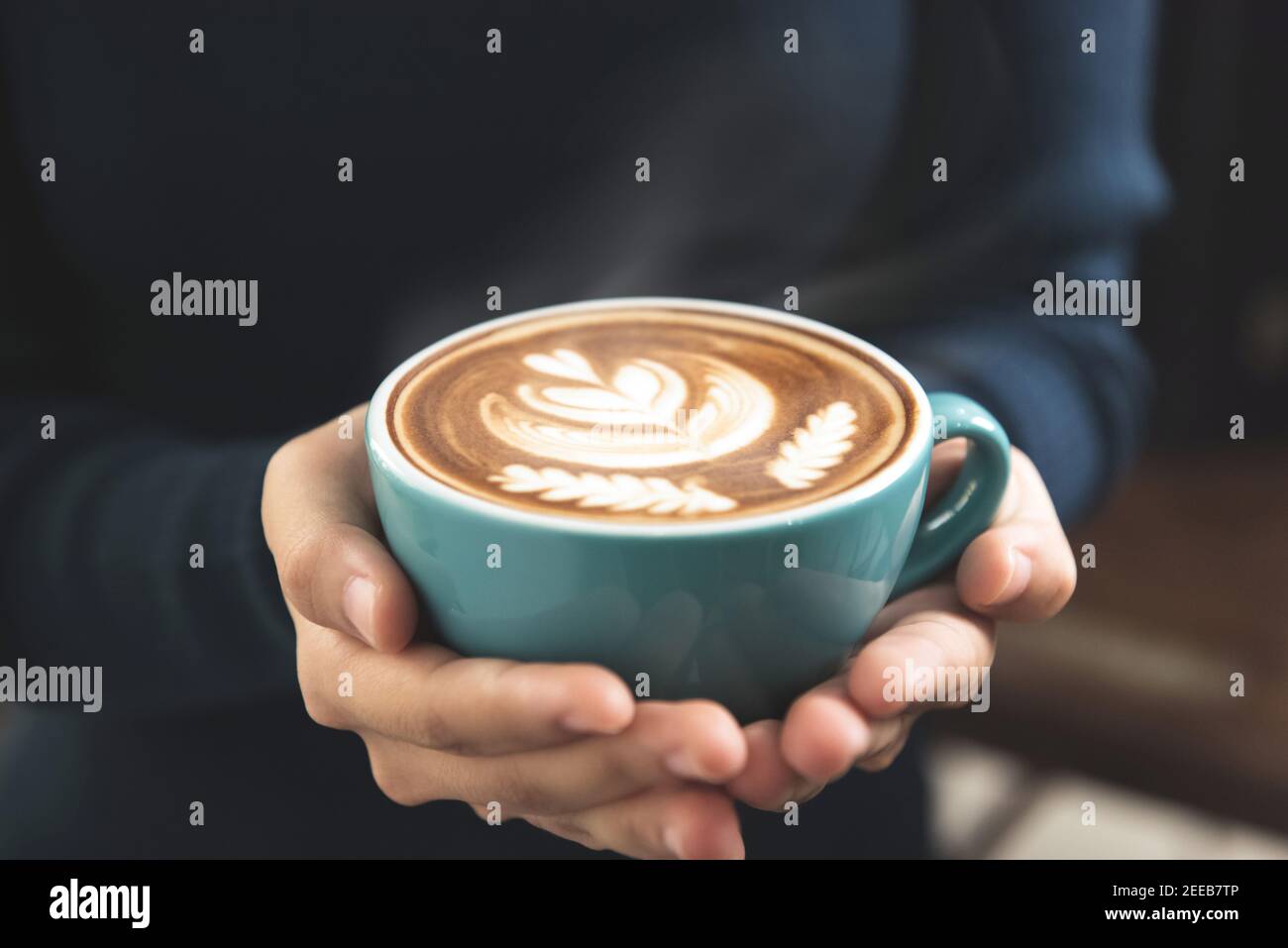 Le mani della donna tengono una tazza di caffè con Rosetta bella motivo latte art sulla superficie Foto Stock