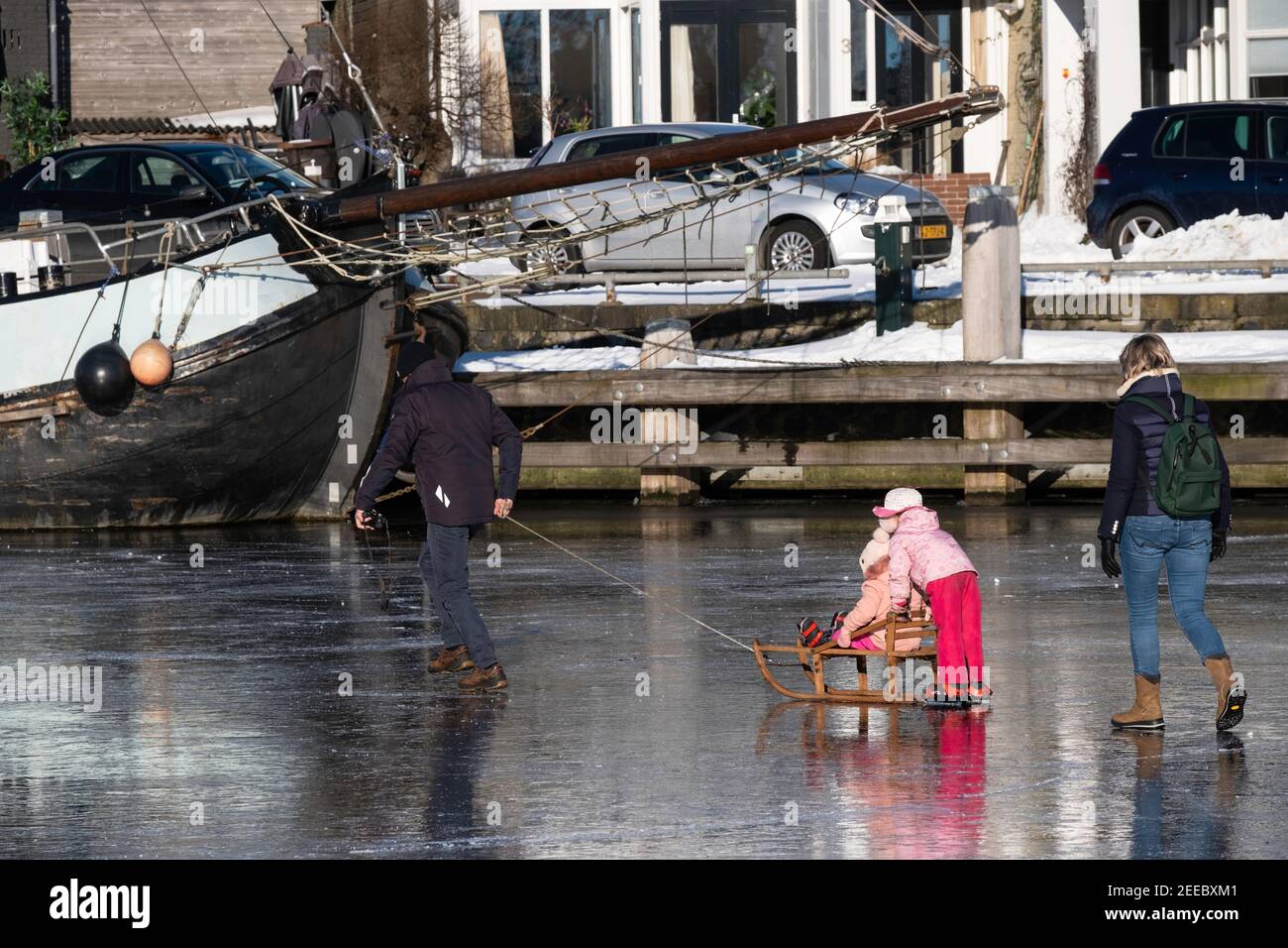 Padre tira le sue figlie su una slitta sul ghiaccio nel porto di Lemmer. Sua moglie cammina dopo di esso. Sullo sfondo una nave congelata nel ghiaccio Foto Stock