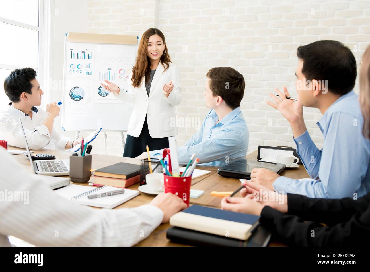 Donna d'affari asiatica leader in un incontro con la sua multietnica colleghi in ufficio che presentano dati di vendita o previsioni per un progetto Foto Stock