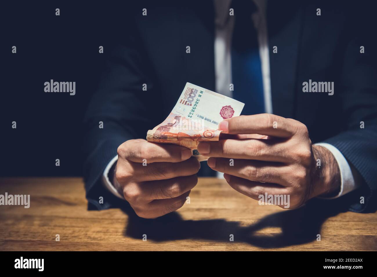 Un uomo d'affari che conta denaro, le banconote russe, sulla sua scrivania in un ufficio buio - corruzione e concetto di corruzione Foto Stock