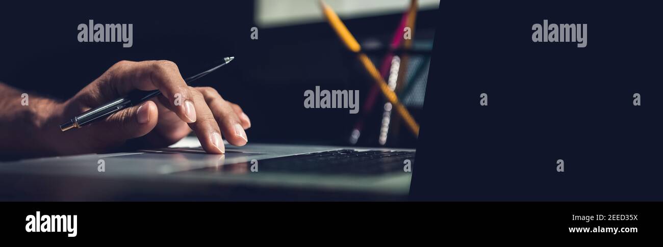 Un uomo che usa un computer portatile che lavora su una nuova idea di progetto alla sua scrivania in ufficio a tarda notte - banner web panoramico con spazio per la copia a destra Foto Stock