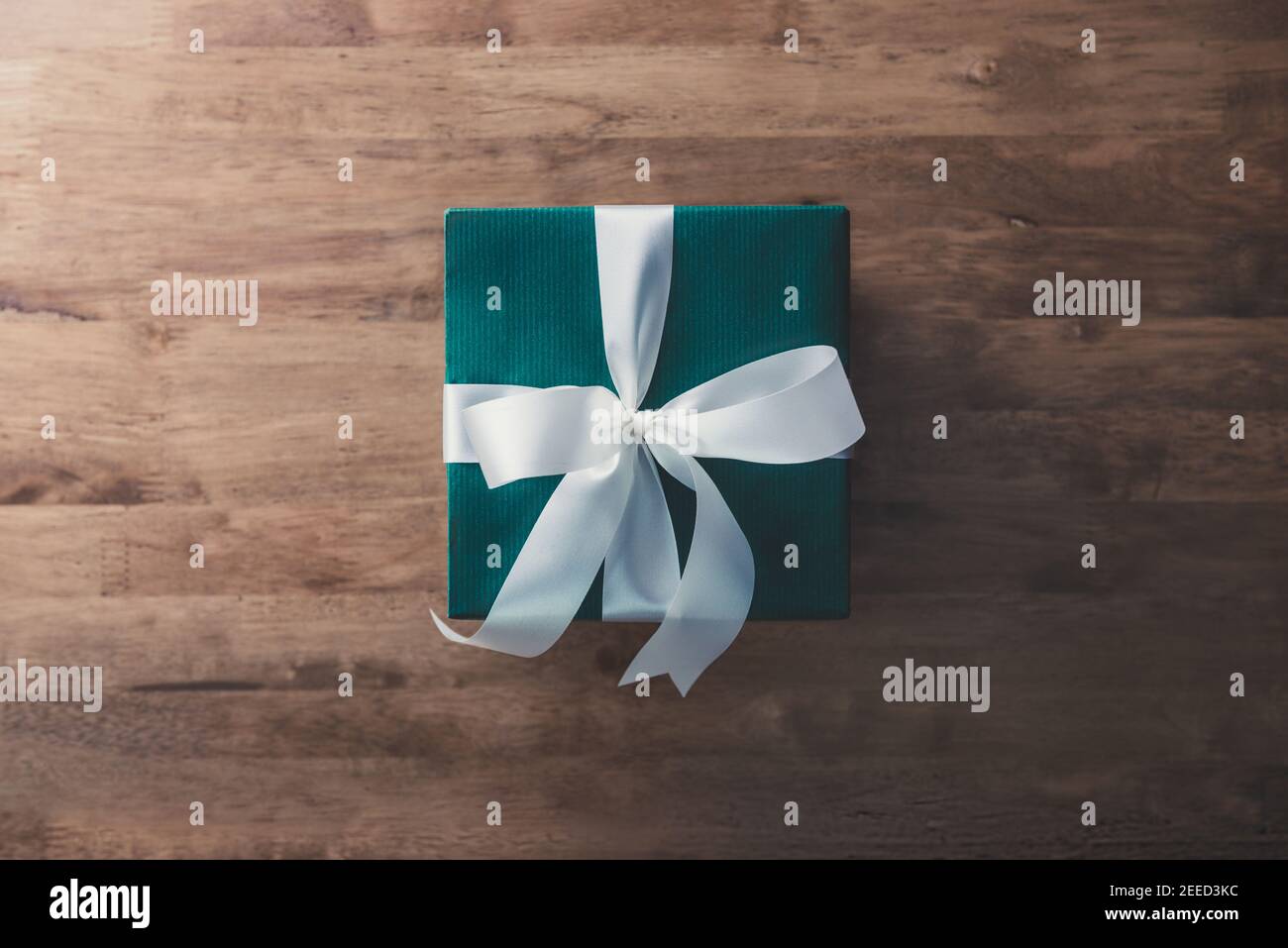 Confezione regalo Natale e Capodanno avvolta di verde carta e nastro bianco inchino su tavola di legno - piano visualizza Foto Stock