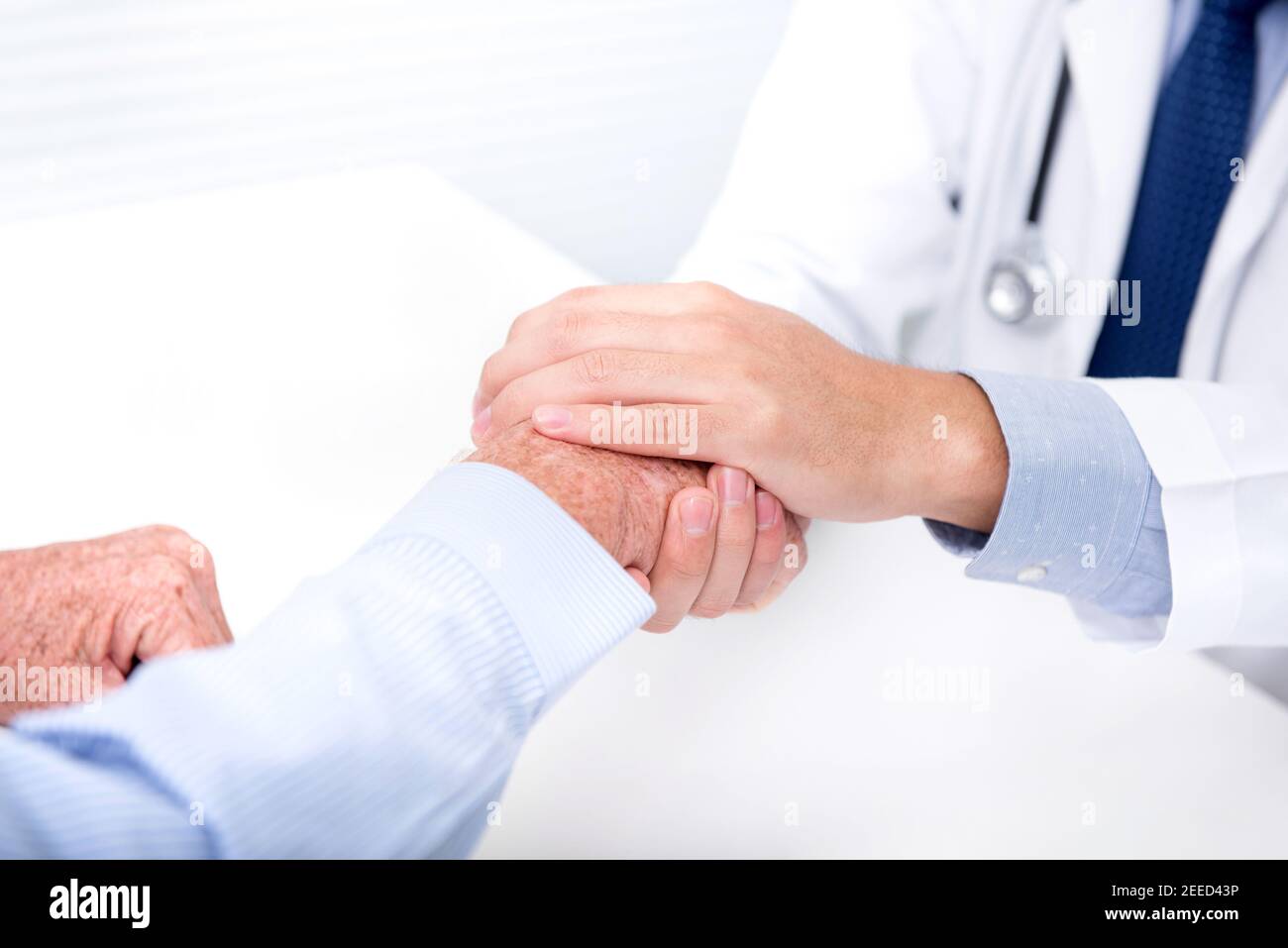 Dottore che conforta un paziente di sesso maschile senior tenendo la mano in ospedale Foto Stock