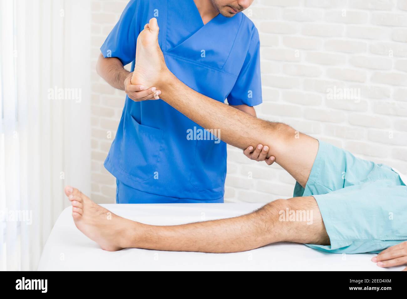 Medico (terapeuta) che tratta la gamba del paziente maschio mentre si sdraiano sul letto in ospedale - concetto di fisioterapia Foto Stock
