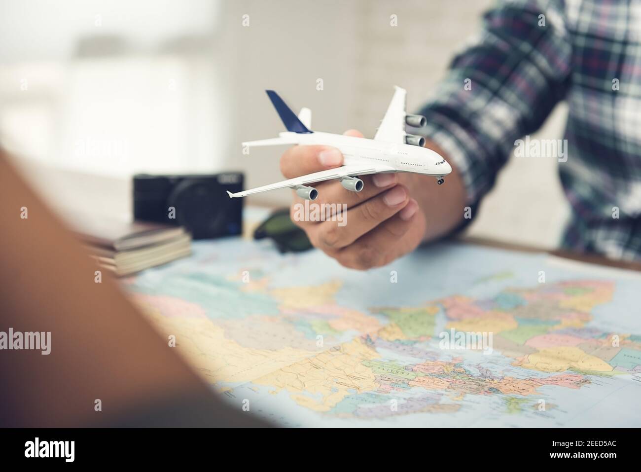 Un uomo che tiene un modello aereo su una mappa del mondo mentre pianifica il viaggio di vacanza a bordo per lui ed il suo socio alle loro destinazioni di sogno Foto Stock