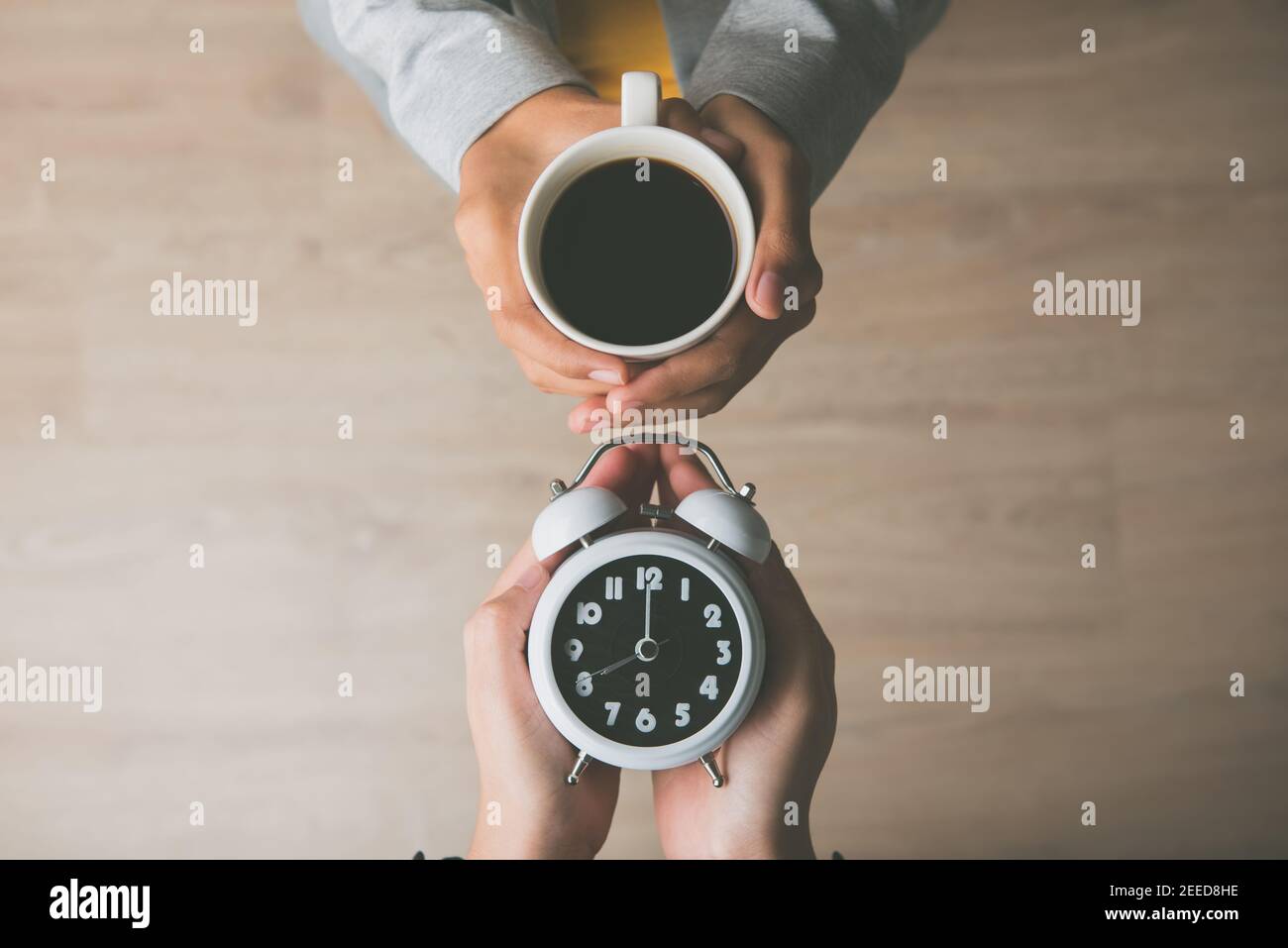 Le mani delle donne che tengono una tazza di caffè e la sveglia indicano che è l'ora di sveglia al mattino, pronto per iniziare la giornata Foto Stock