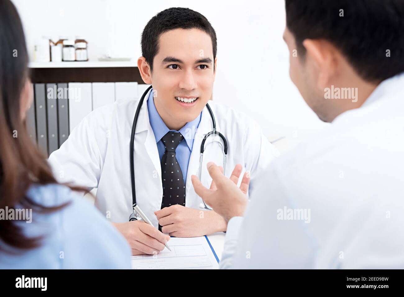 Bel medico di sesso maschile che consulta una coppia circa l'infertilità nel suo ufficio medico Foto Stock