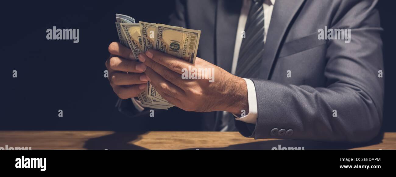Un uomo d'affari che conta soldi, fatture del dollaro USA, in stanza privata oscura - concetto di prestito, pagamento e corruzione, banner panoramico Foto Stock
