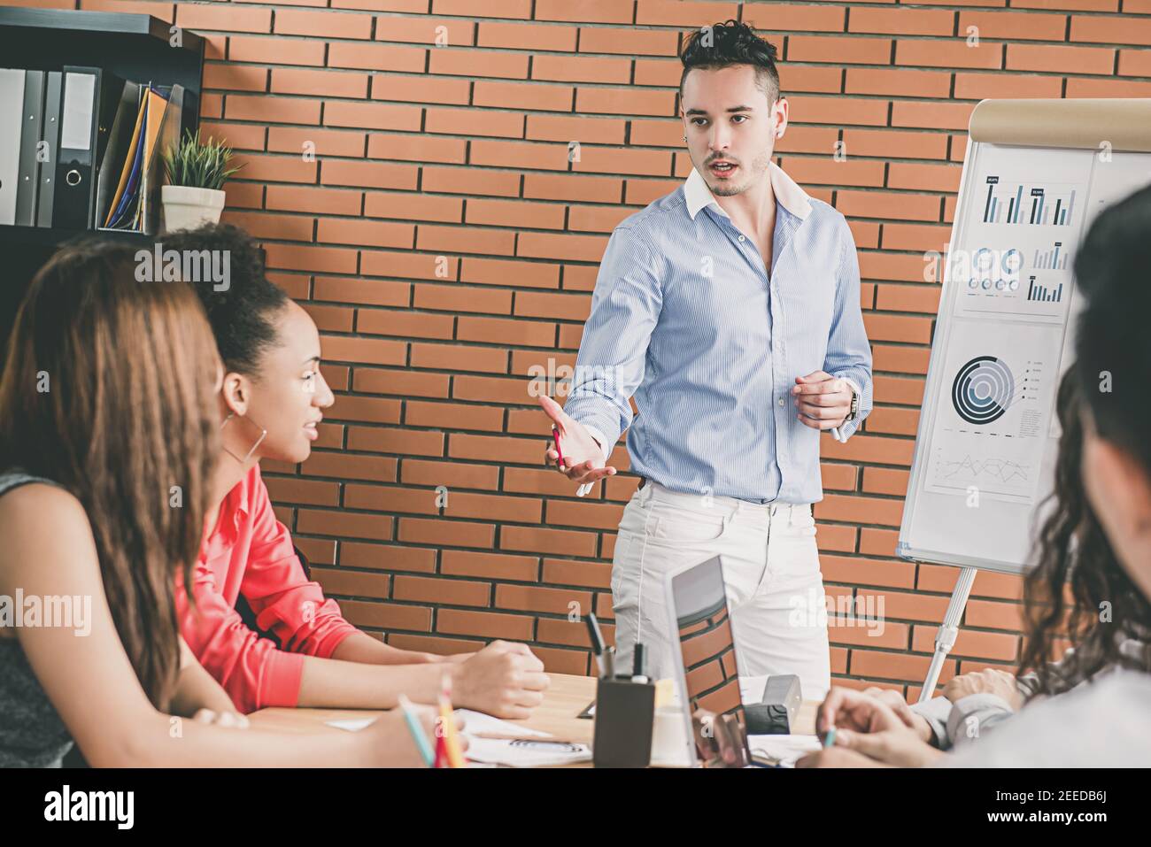Giovane bel capo di un uomo d'affari ispanico che fa una presentazione, condividendo idee e proiezioni con i suoi colleghi in una riunione del team dell'ufficio Foto Stock