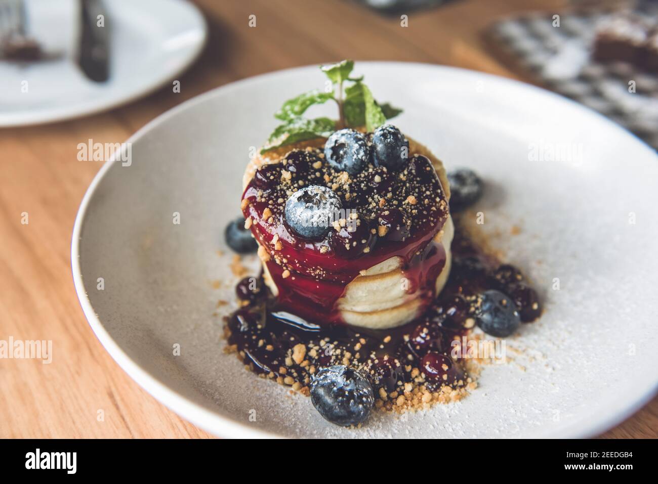 Bella pila appetitosa di frittelle soffici con mirtilli freschi, sciroppo e biscotto macinato in piatto bianco Foto Stock