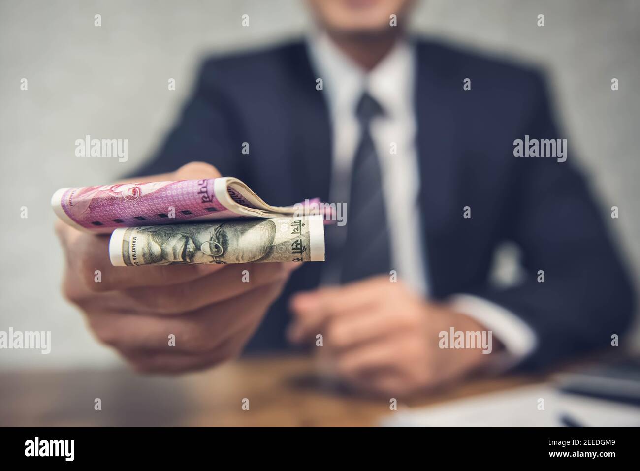 Un uomo d'affari che dà denaro sotto forma di rupee indiane per servizi resi come da un contratto firmato. Foto Stock