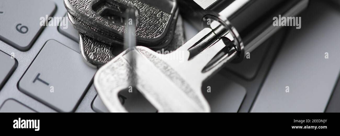 Chiave argentata con lucchetto giace sul retro del closeup della tastiera bianca. Foto Stock