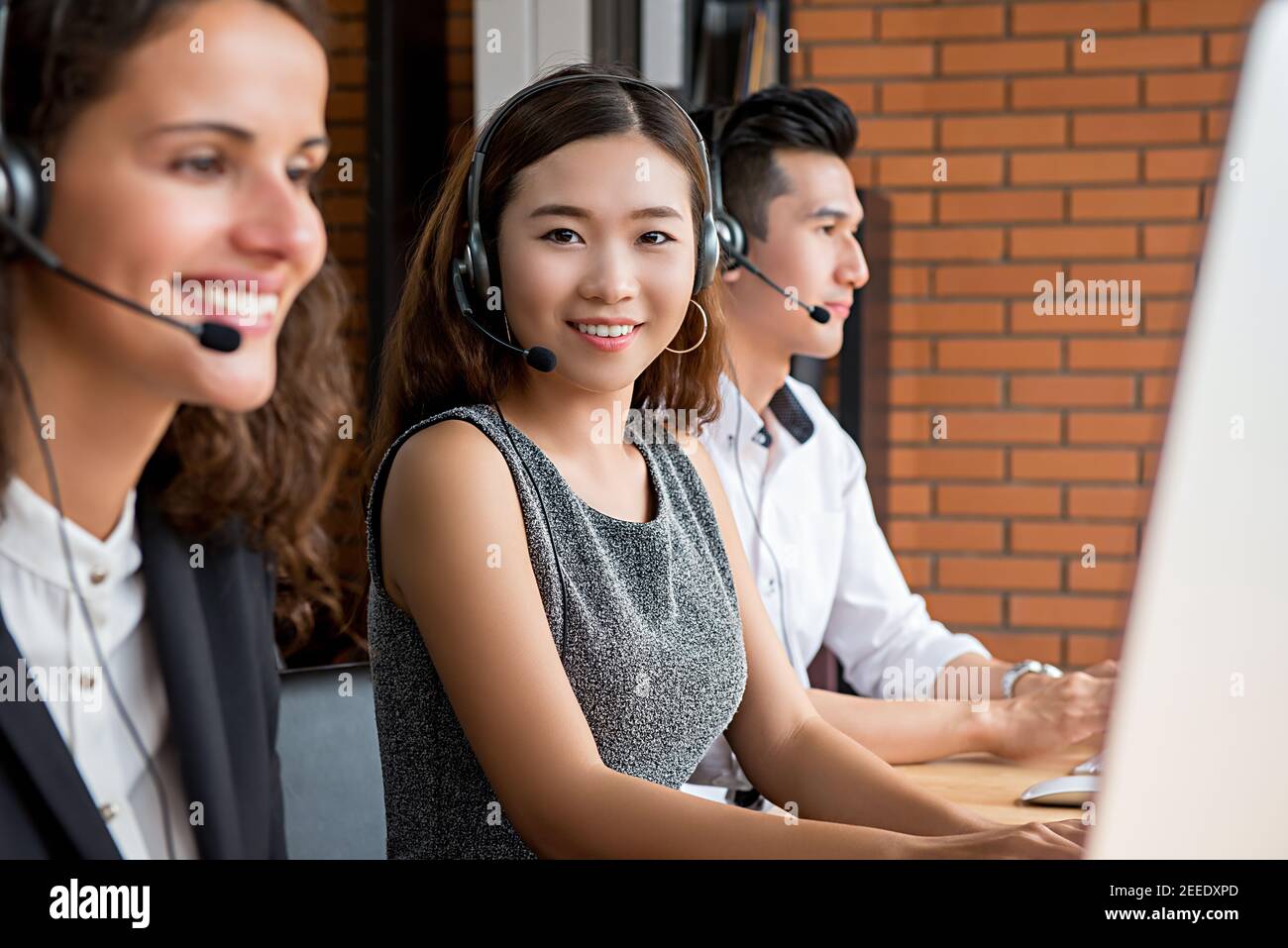Sorridente donna asiatica di telemarketing addetto al servizio clienti che lavora in chiamata centro con team multietnico Foto Stock