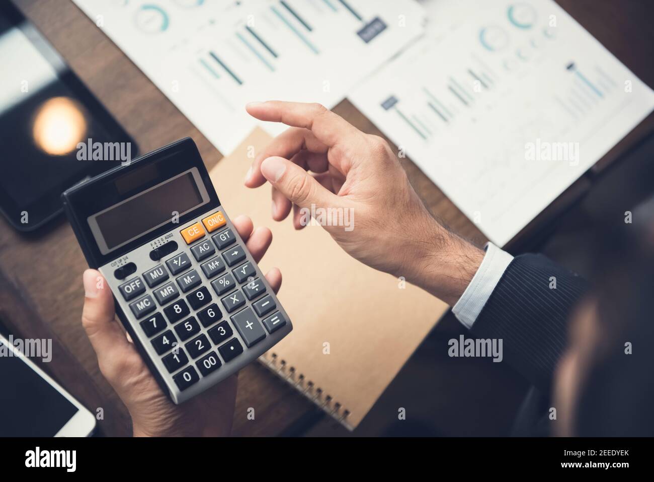 Uomo d'affari o consulente finanziario che utilizza una calcolatrice che calcola e analizza i dati scrivania Foto Stock