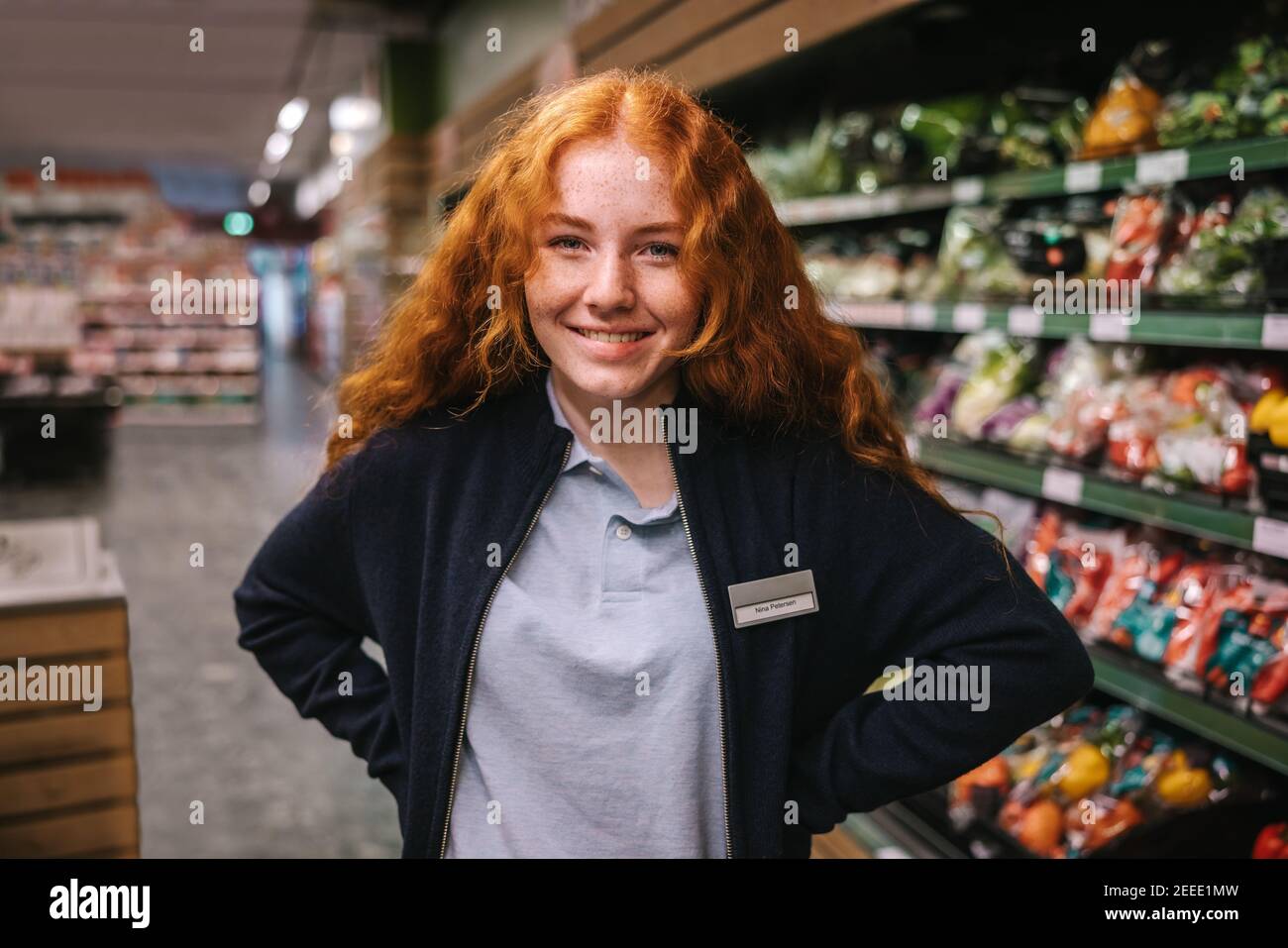 Ritratto di donna in piedi nella corsia del supermercato guardando la macchina fotografica e sorridendo. Donna che lavora in un negozio di alimentari. Foto Stock