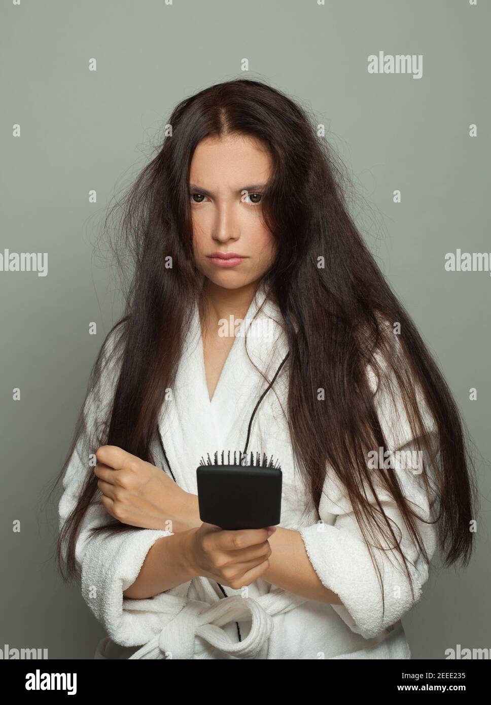 Giovane donna infelice che tiene il pettine su sfondo bianco. Routine di giorno, cura dei capelli e concetto di problema dei capelli Foto Stock