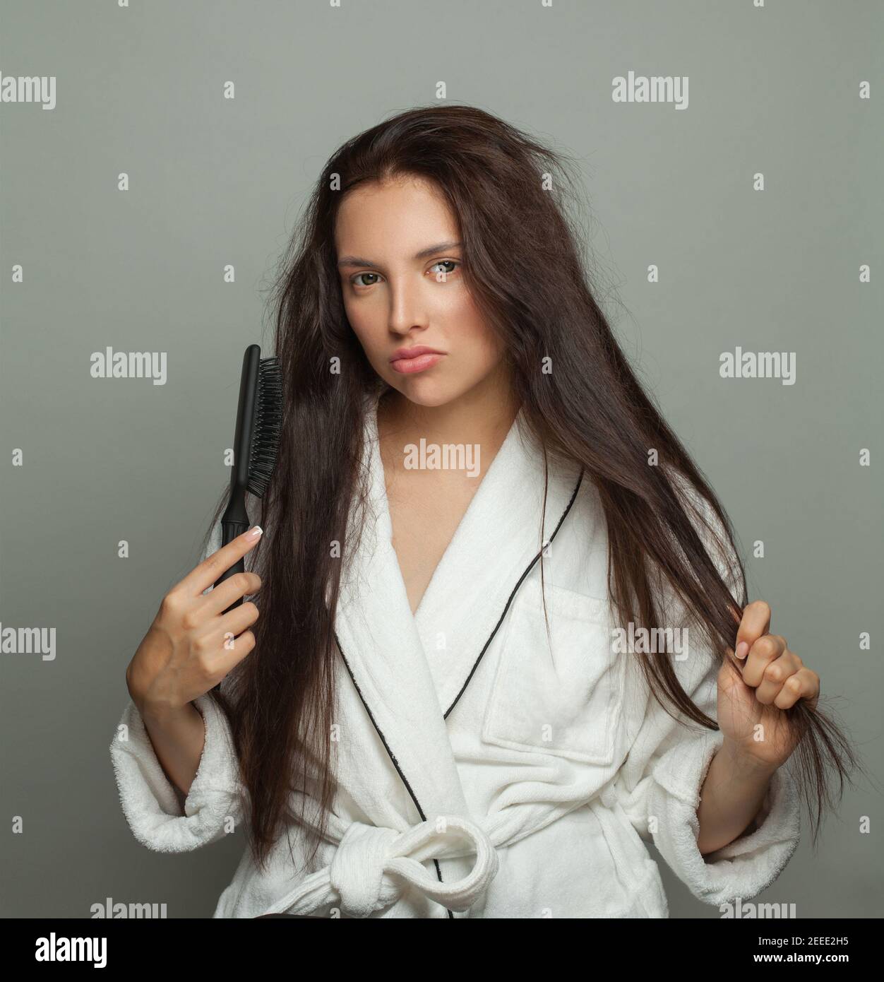 Donna triste che combatte i suoi capelli aggrovigliati su sfondo bianco, cura dei capelli e concetto di problema dei capelli Foto Stock