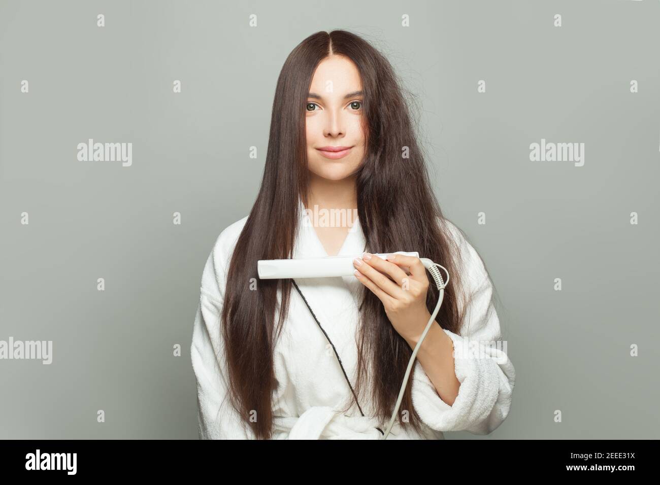 Donna attraente raddrizza i capelli con la piastra su sfondo bianco. Concetto di cura dei capelli Foto Stock