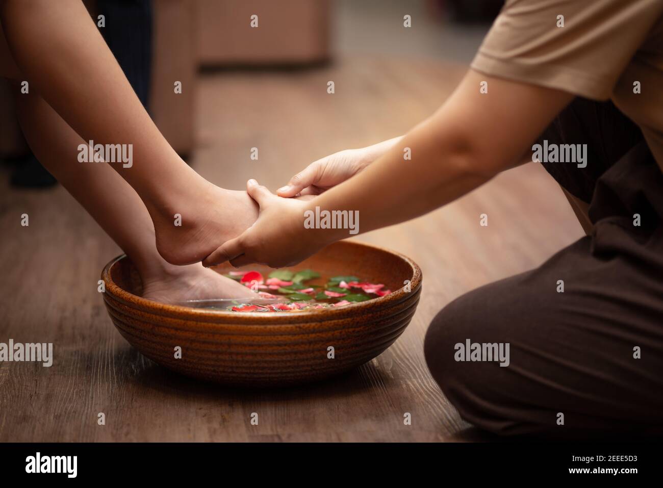 piedi della donna immersi in acqua con petali in una ciotola di legno. Bella femmina piedi al salone spa su pedicure procedura. Foto Stock