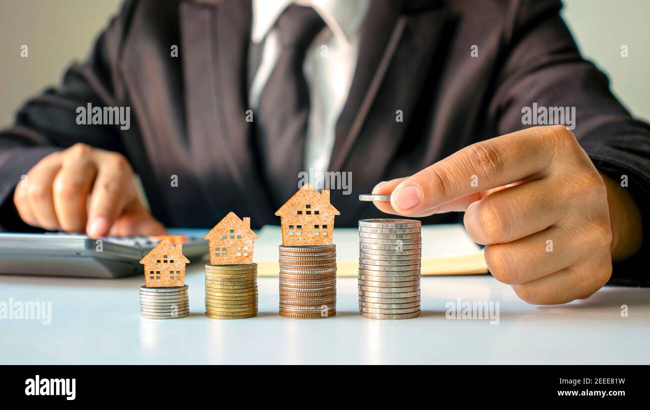 Modello di casa in legno su monete e mani di persone, idee di investimento immobiliare e transazioni finanziarie. Foto Stock